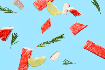 Cut tasty crab sticks with rosemary and slices of lemon flying on blue background © Pixel-Shot
