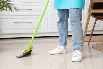 Fototapeta premium Female janitor sweeping floor in kitchen