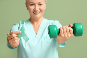 Mature female doctor with teal ribbon and dumbbell on green background. Cervical Health Awareness...