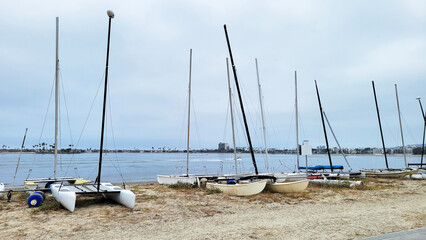 Collection of small catamarans and boats lined up on a sandy beach of Sail Bay, north of San Diego, California