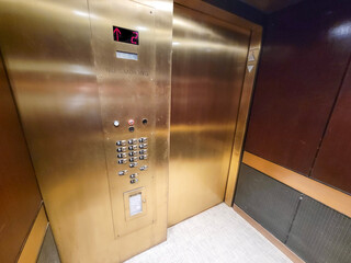
No smoking golden colored elevator with digital panel and push buttons running upstairs