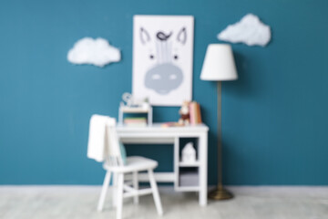 Blurred view of children's room with floor lamp, desk and chair near blue wall
