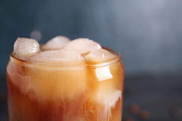Glass of hot coffee with ice cubes on dark background