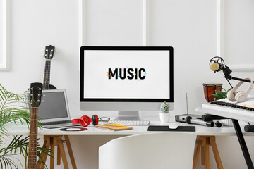 Workplace with computer and musical instruments near light wall in studio