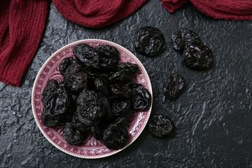 Plate with dried prunes on black background