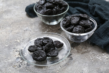Glass bowls and plate with dried prunes on grey background