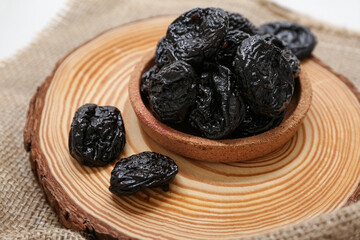 Plate with dried prunes on sack cloth background, closeup