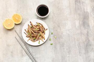 Plate of fried maggots with green onion, lemon and bowl of soy sauce on grey background