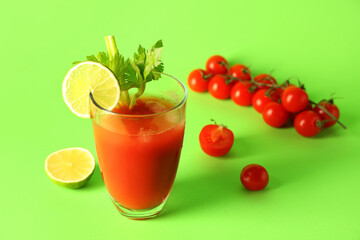 Glass of bloody mary with celery, cut lime and tomatoes on green background