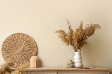 Pampas grass in vase with decor on chest of drawers near white wall in room. Closeup