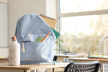 Striped backpack with school stationery and water bottle on desk in classroom