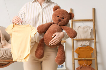 Young woman with baby bodysuit and toy bear at home