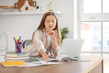 Teenage girl with laptop working online at table in kitchen