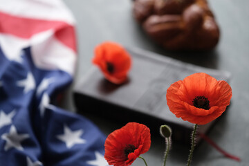 Bright poppy flowers decorated with American flag on a closed bible next to challah bread on a grey...