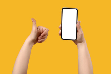 Female hands with blank mobile phone showing thumb-up on yellow background