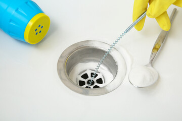 Woman in rubber glove cleaning clogged drain with baking soda and plumber's snake, closeup