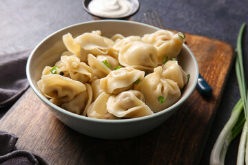 Bowl of delicious boiled dumplings with green onion and sour cream on dark background, closeup