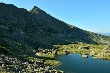 The shadow of the rising sun from a high cliff barely touches the edge of a beautiful lake in a picturesque mountain valley.