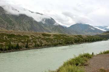 Thunderclouds low over a picturesque mountain valley with a beautiful river flowing through it on a sunny summer day.