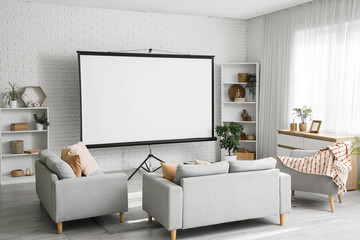 Interior of living room with sofa, armchairs, shelving units and projector screen near white brick wall
