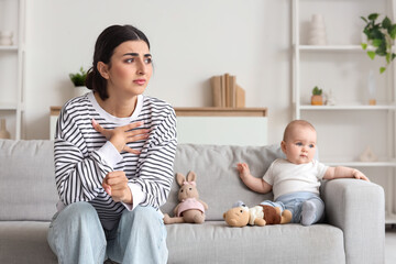 Young mother suffering from postnatal depression with her baby on sofa at home