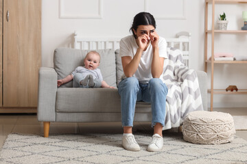 Crying mother suffering from postnatal depression with her baby on sofa at home