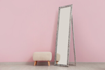 Floor mirror and pouf near pink wall in room