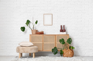 Interior of modern living room with chest of drawers, pouf and Monstera houseplants