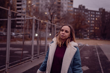 Fototapeta premium Young woman looking up in an urban park during twilight, surrounded by city buildings and a quiet track