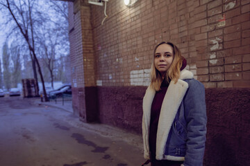 A young woman stands in a narrow, dimly lit alleyway lined with brick walls.