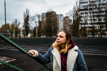 A young woman poses confidently on a staircase in an urban setting, showcasing her stylish winter...