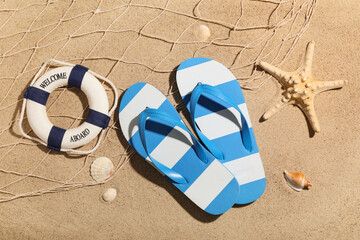Composition with stylish flip-flops, net and decorative lifebuoy on sand as background, closeup