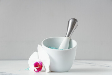 Mortar with sea salt, pestle and orchid flower on table against grey wall