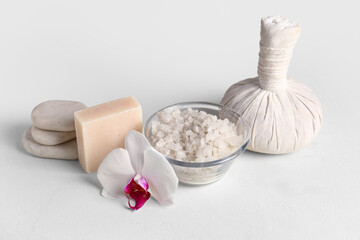 Spa composition with bowl of sea salt, massage bag and soap on light background