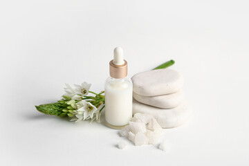 Bottle of essential oil, spa stones, sea salt and flower on light background
