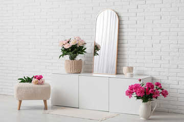 Pouf, chest of drawers, mirror and beautiful peony flowers in interior of room