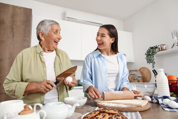 Happy young woman with her grandmother rolling out dough in kitchen