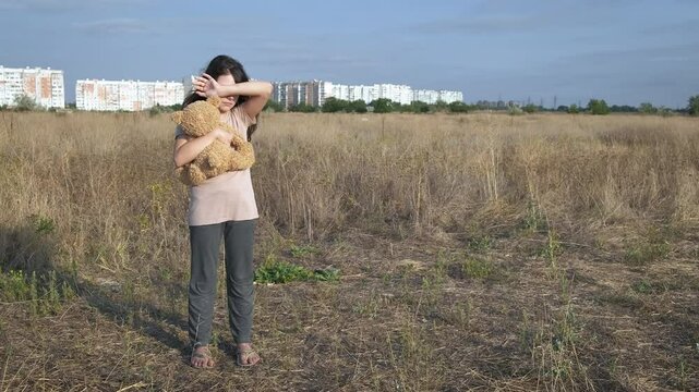 Abadoned little girl with toy outdoor. A view of empty place with abandoned child with teddy bear during day time.
