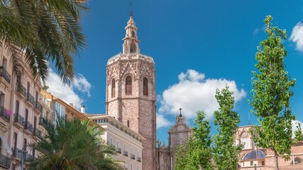 Panoramic timelapse of Plaza de la Reina in Valencia, Spain. Lively square with a historic church tower, bustling cafes and a central fountain under the warm Mediterranean cloudy sky.