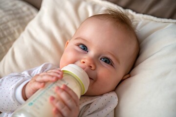 A joyful baby happily enjoying a bottle while resting on soft pillows, showcasing innocence and comfort.