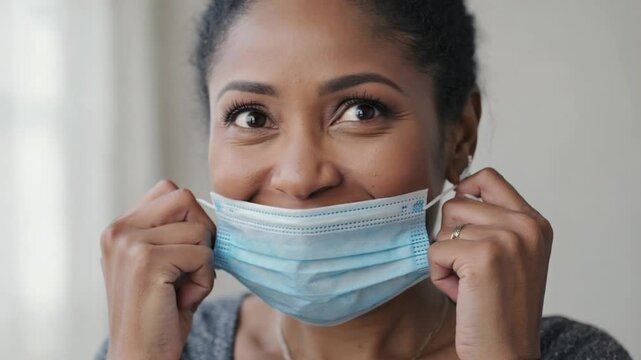 A young woman removing a medical face mask and smiling, symbolizing freedom, relief, and post-pandemic normalcy.
