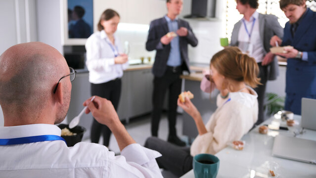 Staff lunch in the office kitchen of the family office. A group of people are eating salads and sandwiches and drinking coffee. Business lunch
