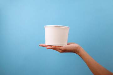 Hand Presenting White Paper Bowl Or Disposable Cup Against Blue Background