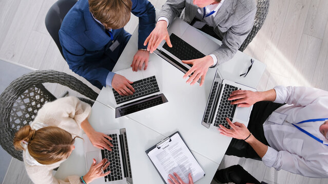 A consulting firm is working on a major project, top view. A group of people are sitting at a table with their laptops open