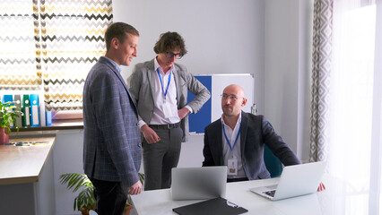 The personable, serious head of the company asks his subordinates for a progress report. Three men in business suits are discussing an important project