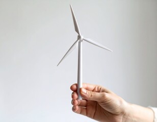 Mano sosteniendo una turbina eólica en miniatura, simbolizando sostenibilidad, innovación y energía limpia.