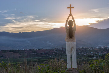 Young Christian Girl with cross Praying Outside at Sunset on a Summer Day. Rear view