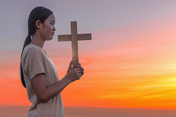 Young Christian Girl with cross Praying Outside at Sunset on a Summer Day