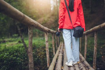 A girl holding binoculars walking on a bridge in the forest.Rear view