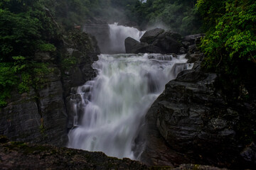 Powerful Borhill  waterfall cascading over dark rocks amidst lush green foliage.